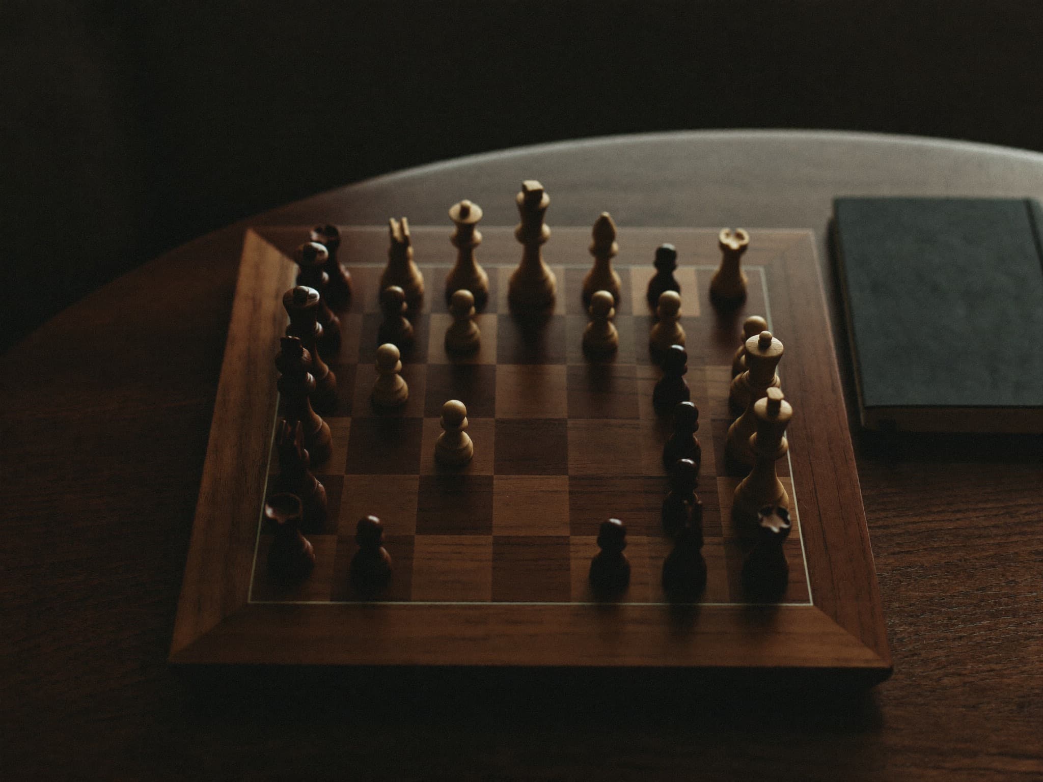 A wooden chess board mid-game on a walnut desk